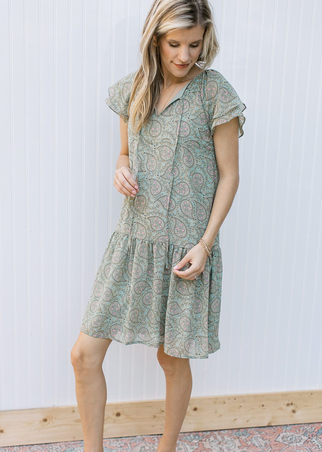 Model wearing a sage above the knee dress with a paisley design and a v-neck with a tie.