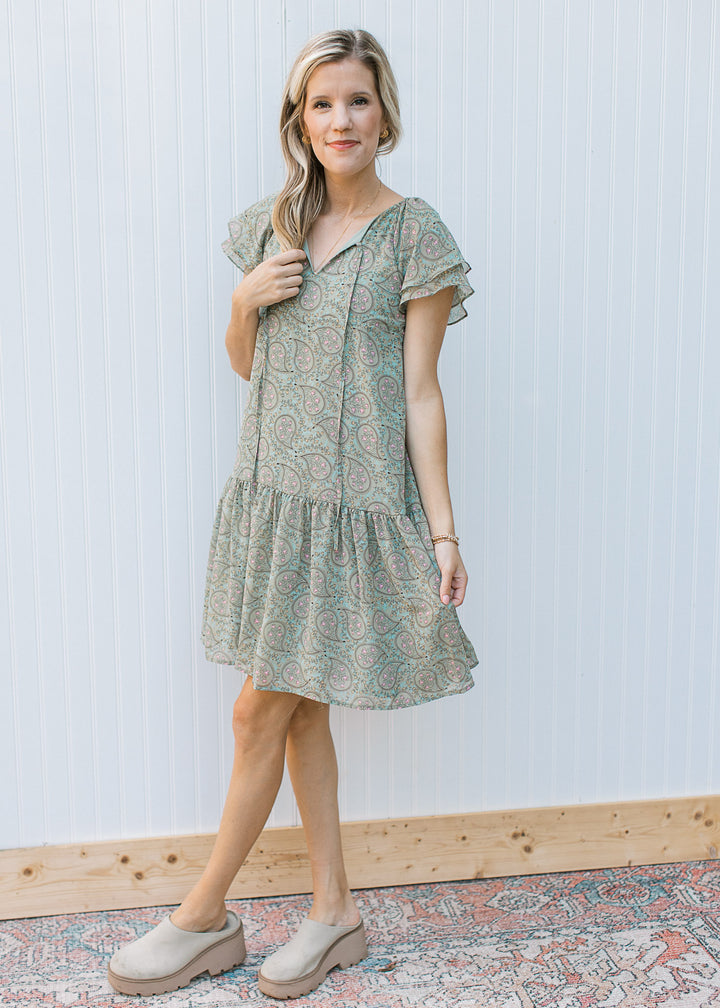 Model wearing mules with a sage dress with paisley design, layered short sleeves and v-neck.