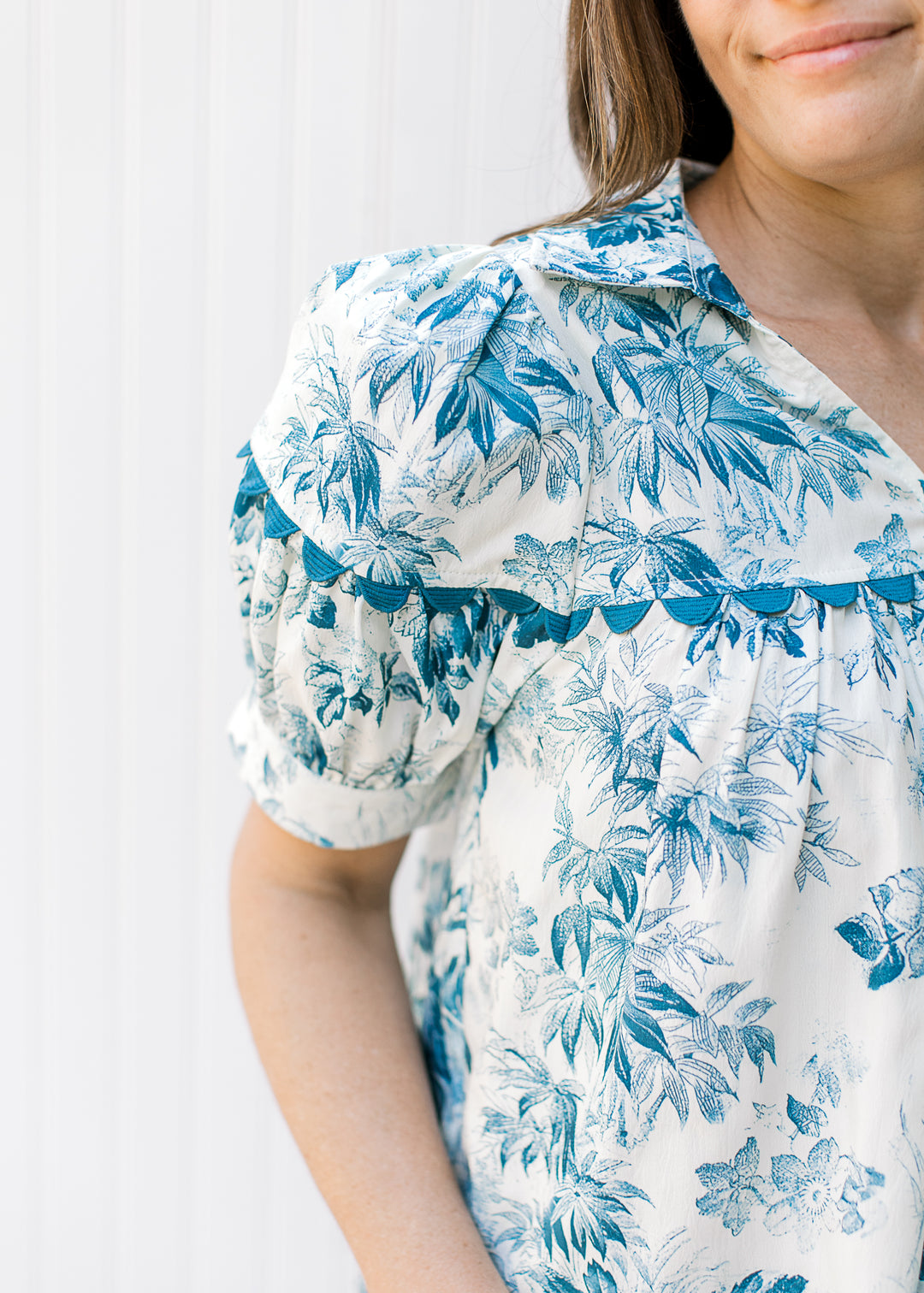 Close up of scallop detail and collar on a cream top with teal flowers.