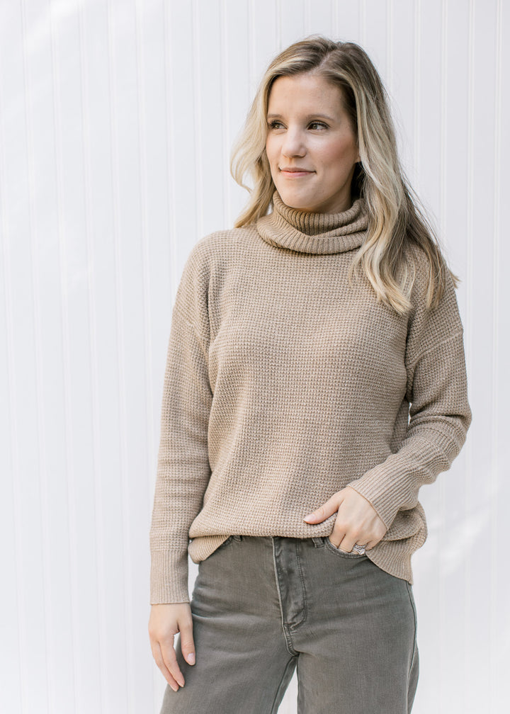 Model wearing a taupe sweater with a loose turtle neck and ribbed collar, hem and cuff.