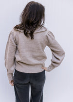 Back view of Model wearing a taupe sweater with an exaggerated collar and long sleeves. 