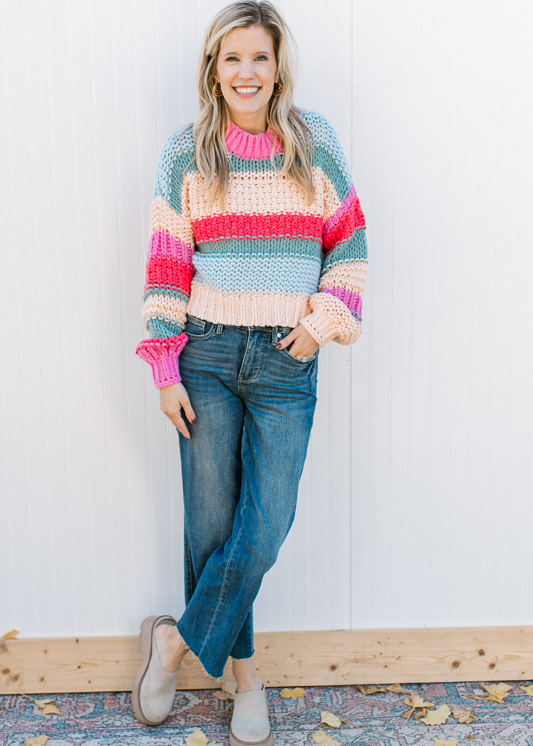 Model wearing jeans, mules and a chunky color block sweater with long sleeves and a round neck.