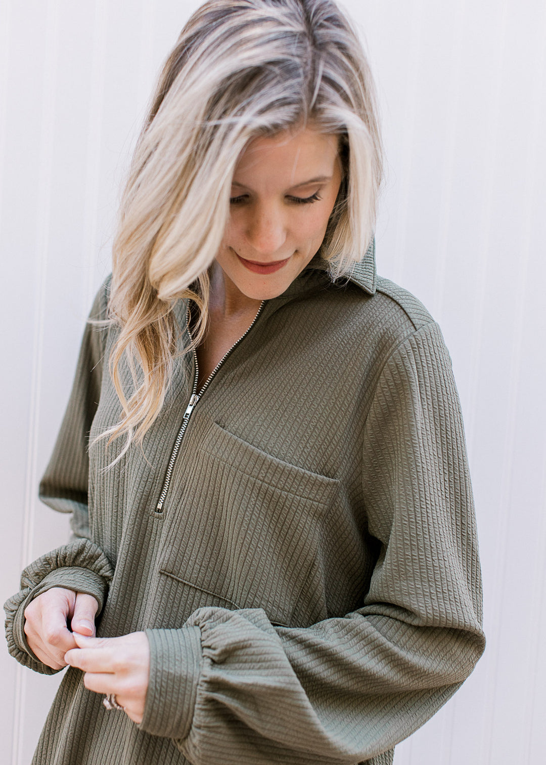 Close up of quarter zip, flap collar and patch pocket on a long sleeve ribbed olive midi.