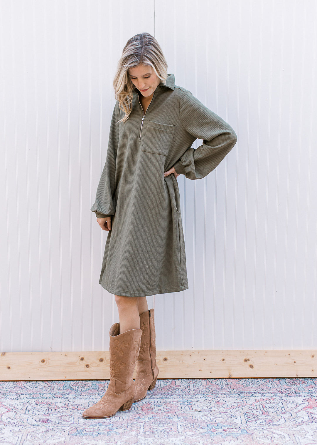 Model wearing an olive ribbed midi with a quarter zip neck, bubble long sleeves and a patch pocket.