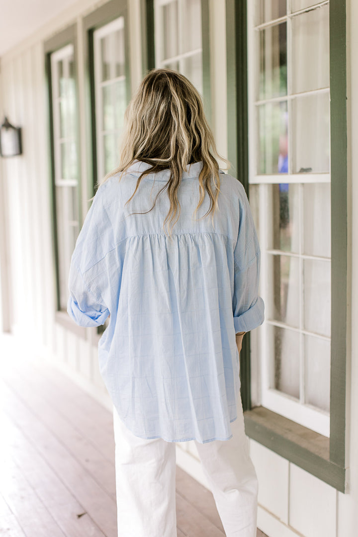 Back view of Model wearing a light blue button down top with a patch pockets and long sleeves.
