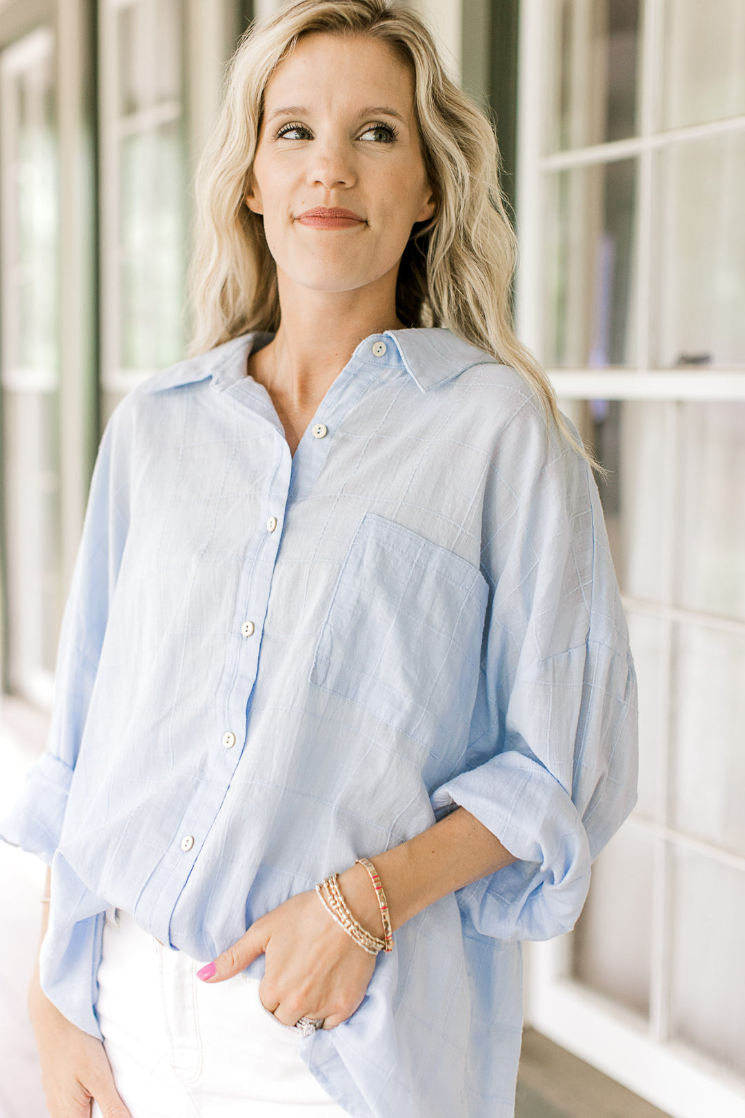 Model wearing a light blue button down top with a patch pockets and long sleeves.