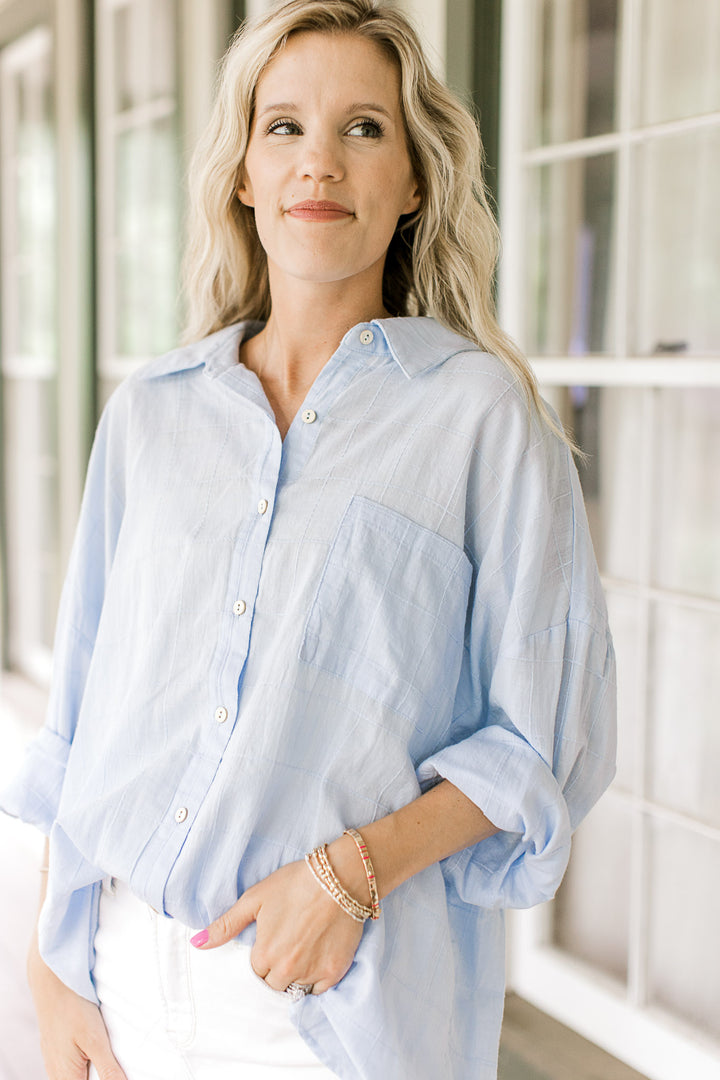 Model wearing a light blue button down top with a patch pockets and long sleeves.