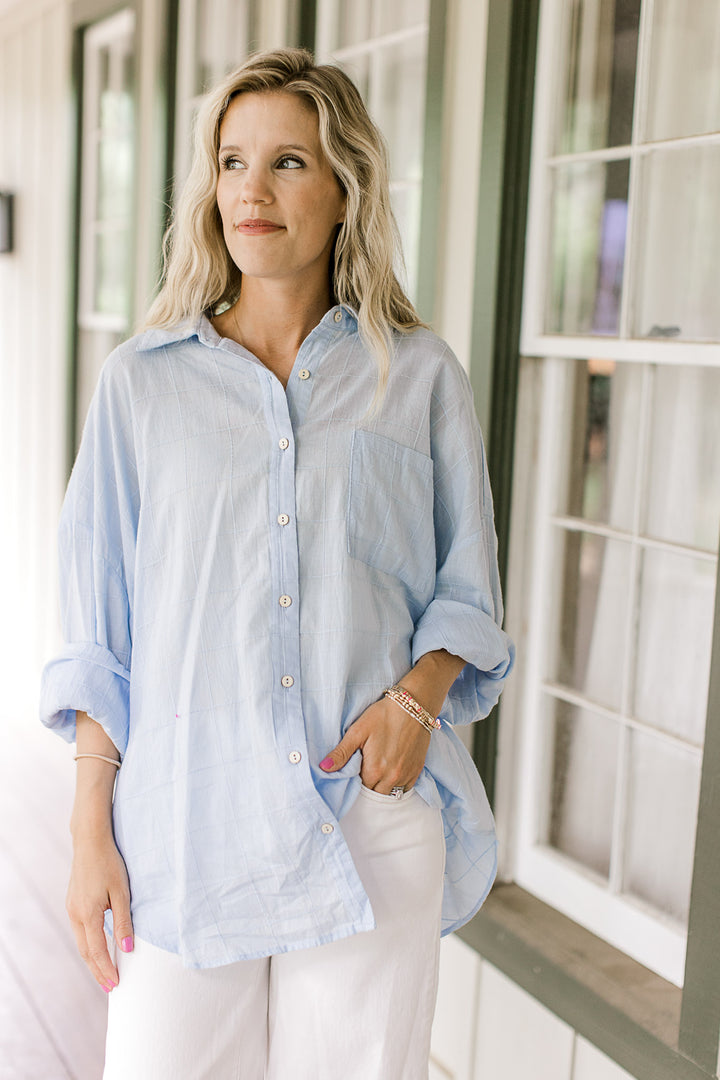 Model wearing white pants with a light blue button down top with a patch pockets and long sleeves.