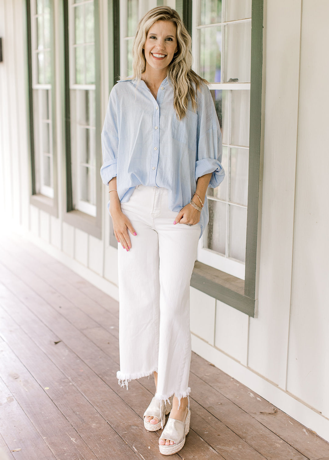 Model wearing white pants and wedges with a light blue top with a patch pockets and long sleeves.