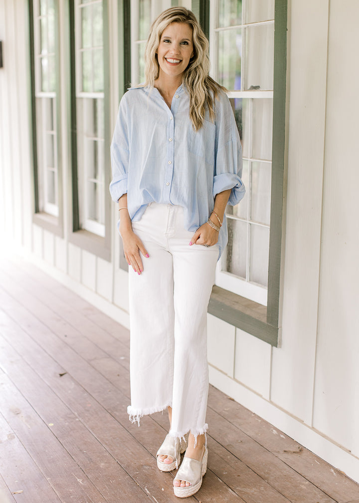 Model wearing white pants and wedges with a light blue top with a patch pockets and long sleeves.