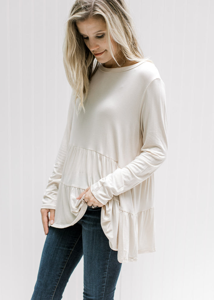 Model wearing a cream tiered top with long sleeves, a round neck and composed of bamboo viscose.