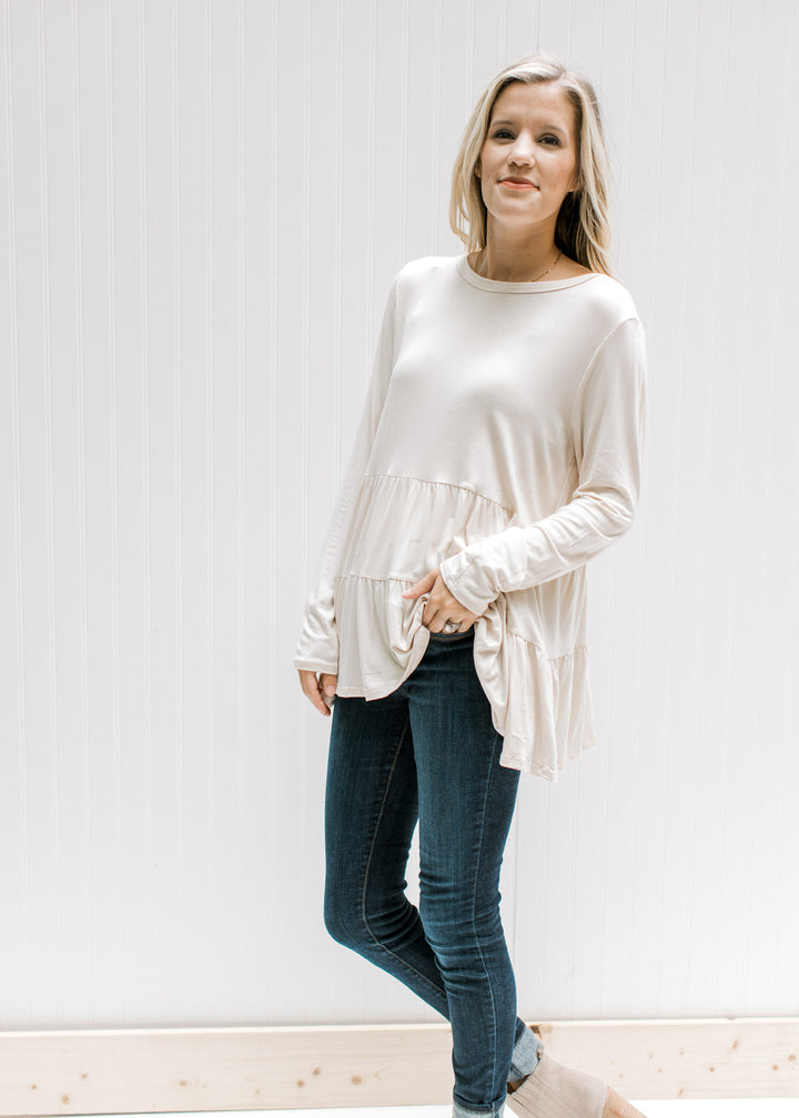 Model wearing jeans with a cream tiered top with long sleeves and composed of bamboo viscose.
