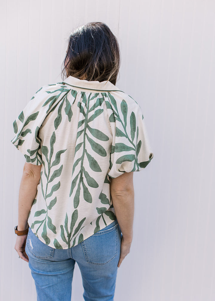Back view of Model wearing a cream top with olive print, bubble short sleeves and a collar.