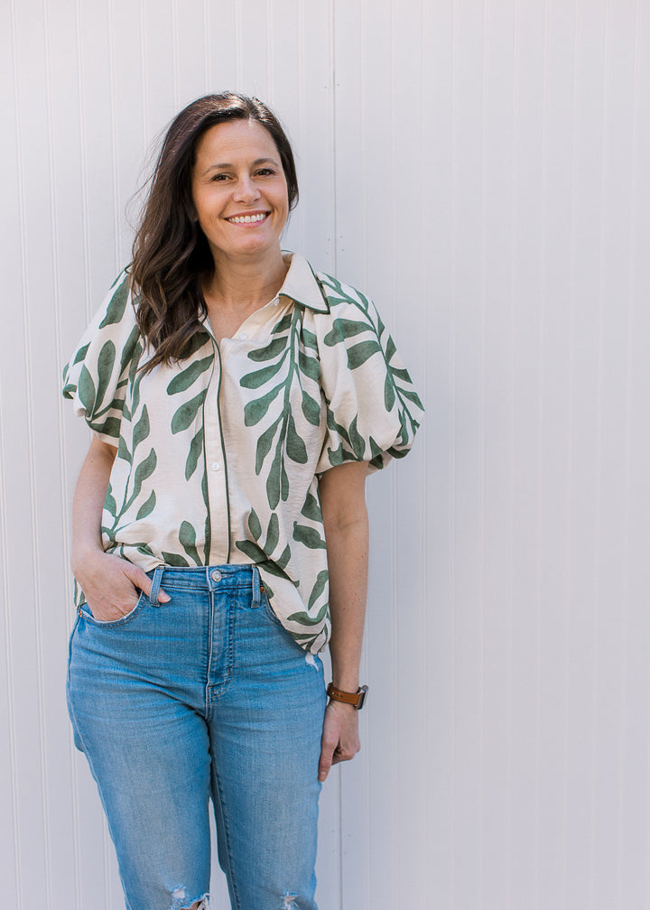 Model wearing jeans and a cream top with olive print, bubble short sleeves and button closure.
