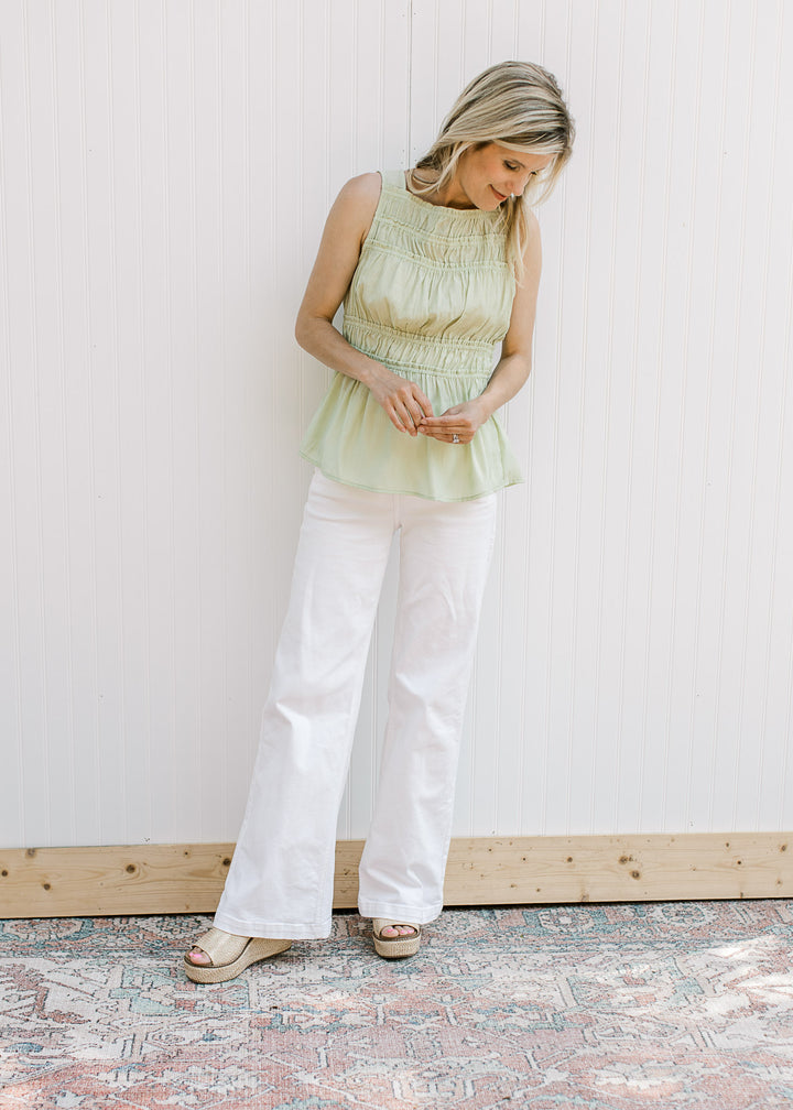 Model wearing white jeans, wedges and a soft green top with elastic pleat at waist and bodice.
