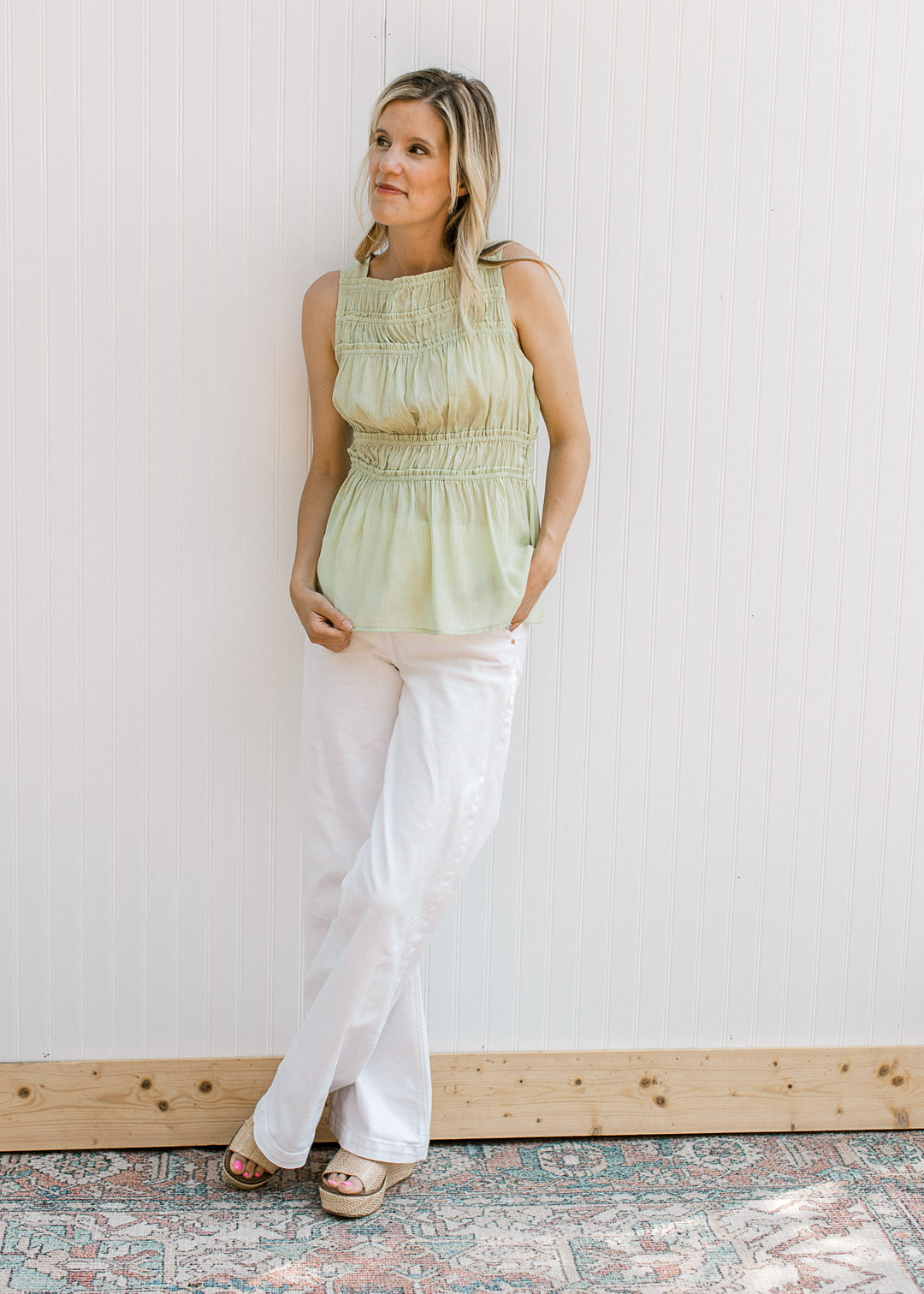 Model wearing a sleeveless soft green top with an crinkle fabric and elastic at waist and bodice.