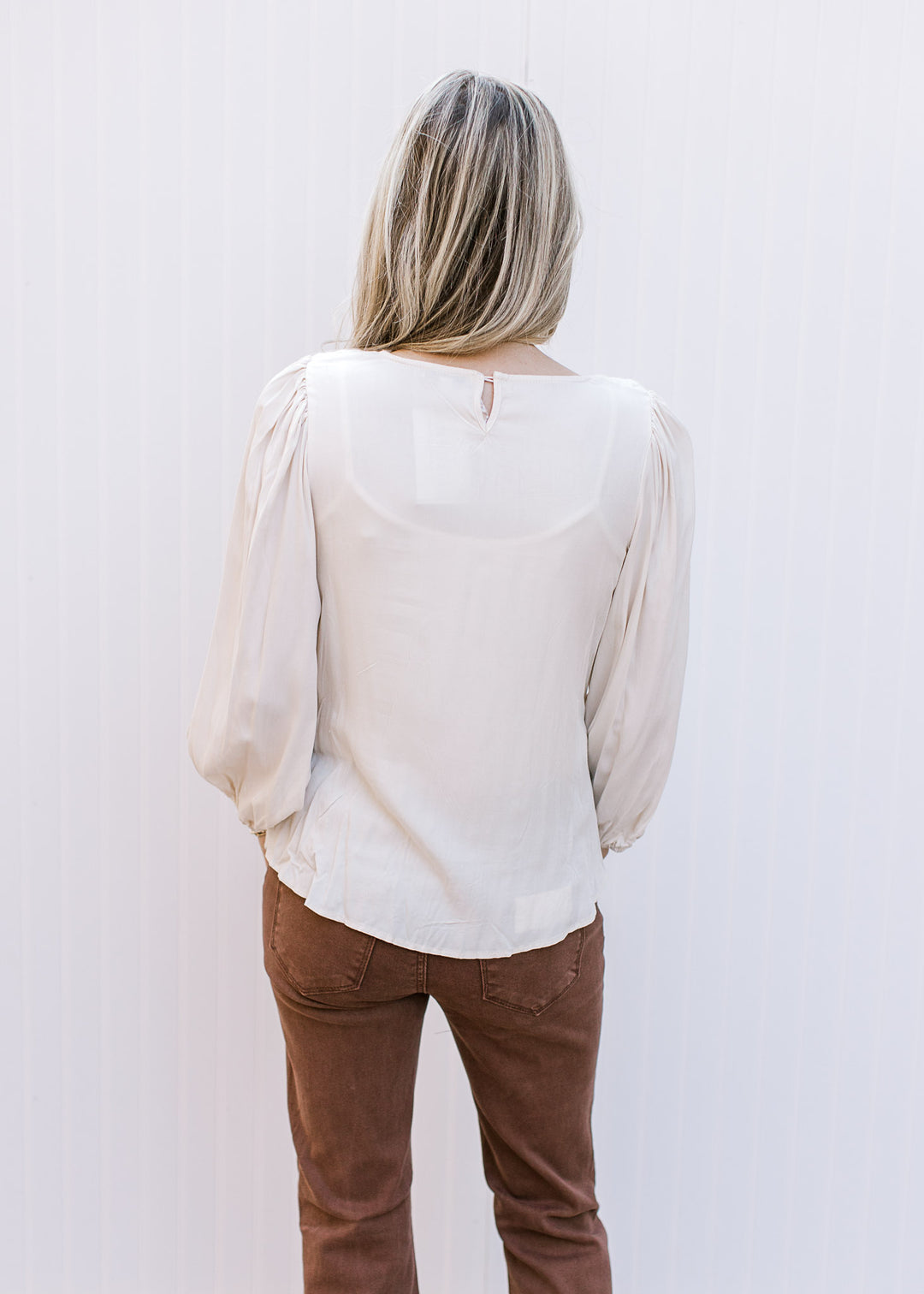 Back view of Model wearing a cream top with crochet front, pleated shoulders and keyhole closure.