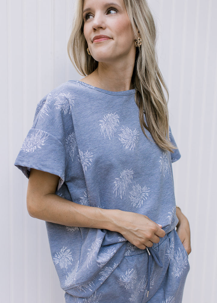 Model wearing a denim color top with light blue dandelions, short sleeves and a round neck.