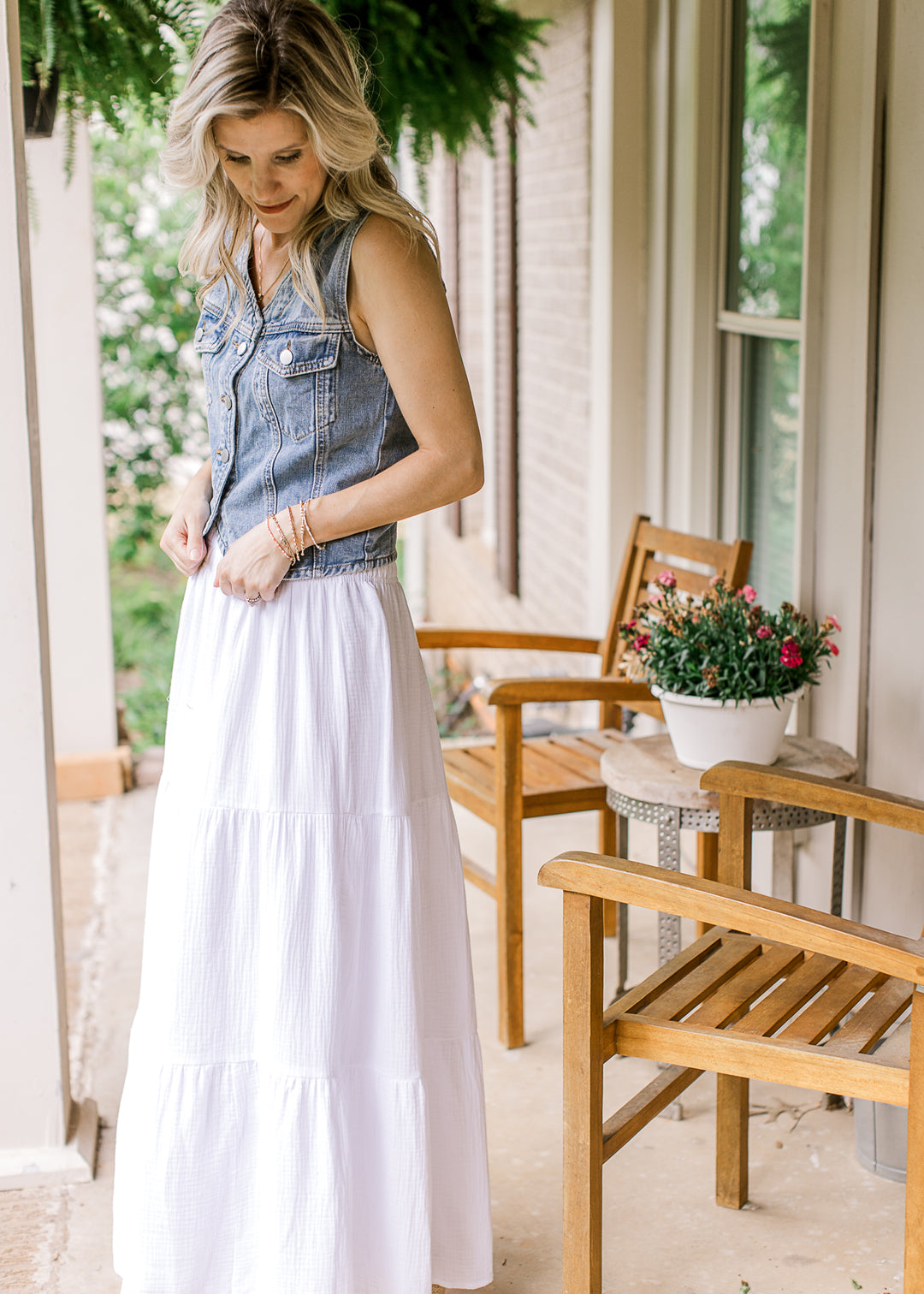 Model wearing a white skirt and a medium wash denim vest with a button closure and patch pockets.