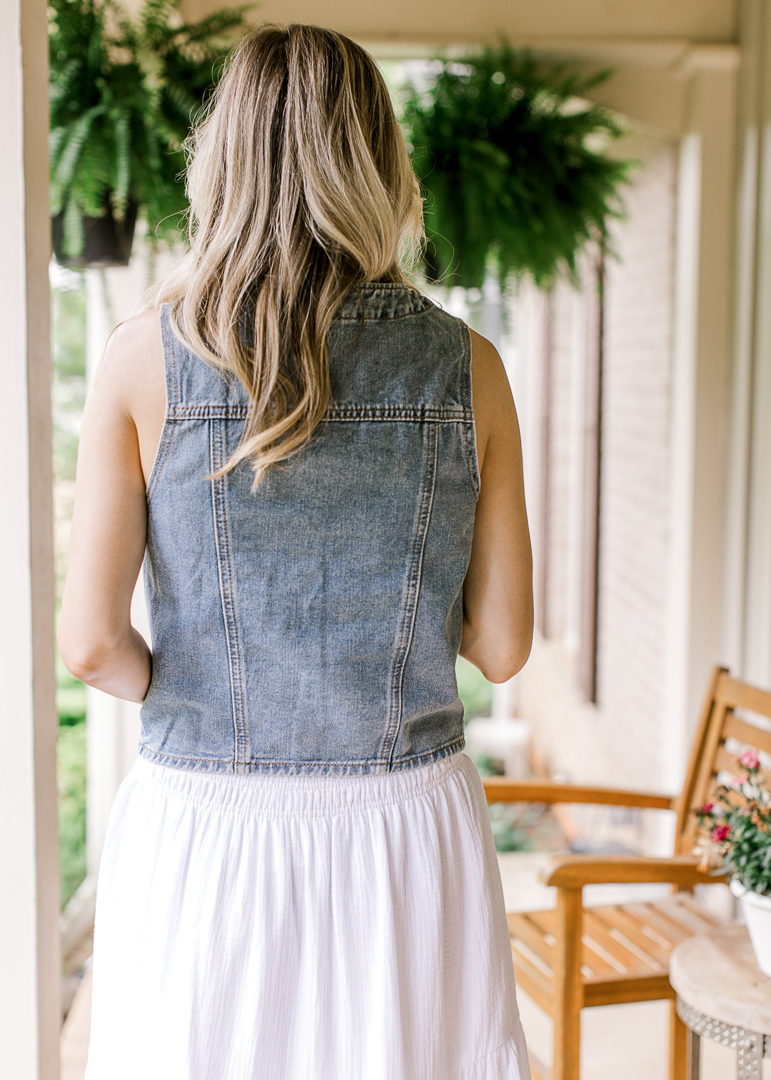 Back view of Model wearing a medium wash denim vest with a V-neck and patch pockets.