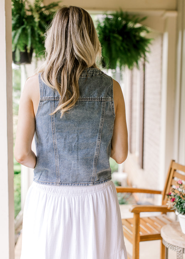 Back view of Model wearing a medium wash denim vest with a V-neck and patch pockets.