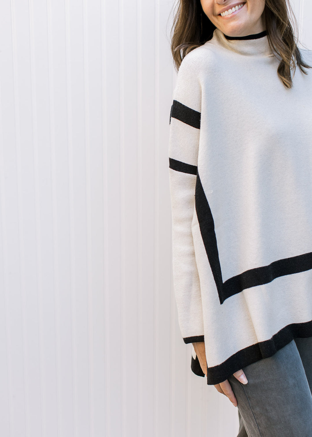Model wearing a cream sweater with black outline, mocked neck and long sleeves.