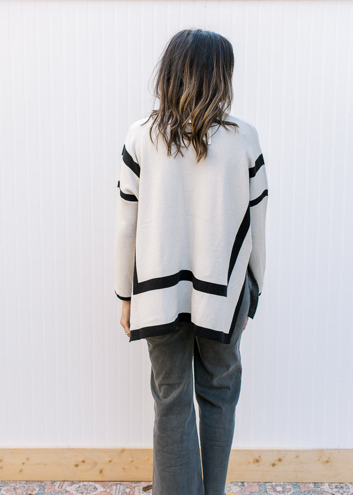 Back view of Model wearing a cream sweater with black outline, mocked neck and long sleeves.