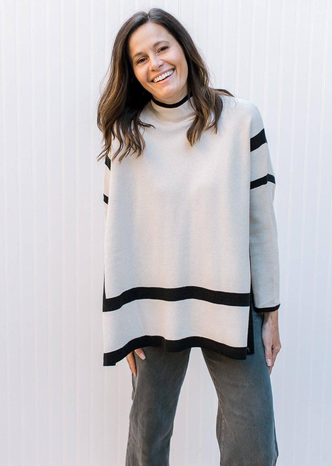 Model wearing jeans with a cream sweater with black outline, mocked neck and long sleeves.