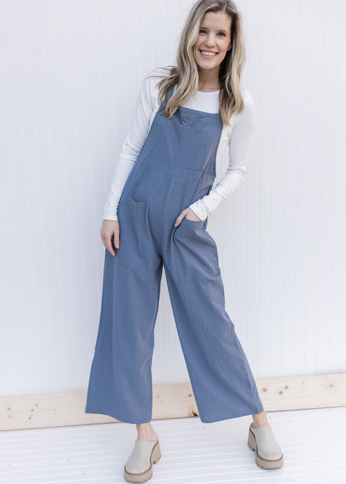 Model wearing a dusty blue jumpsuit with front patch pockets and wide leg bottoms. 