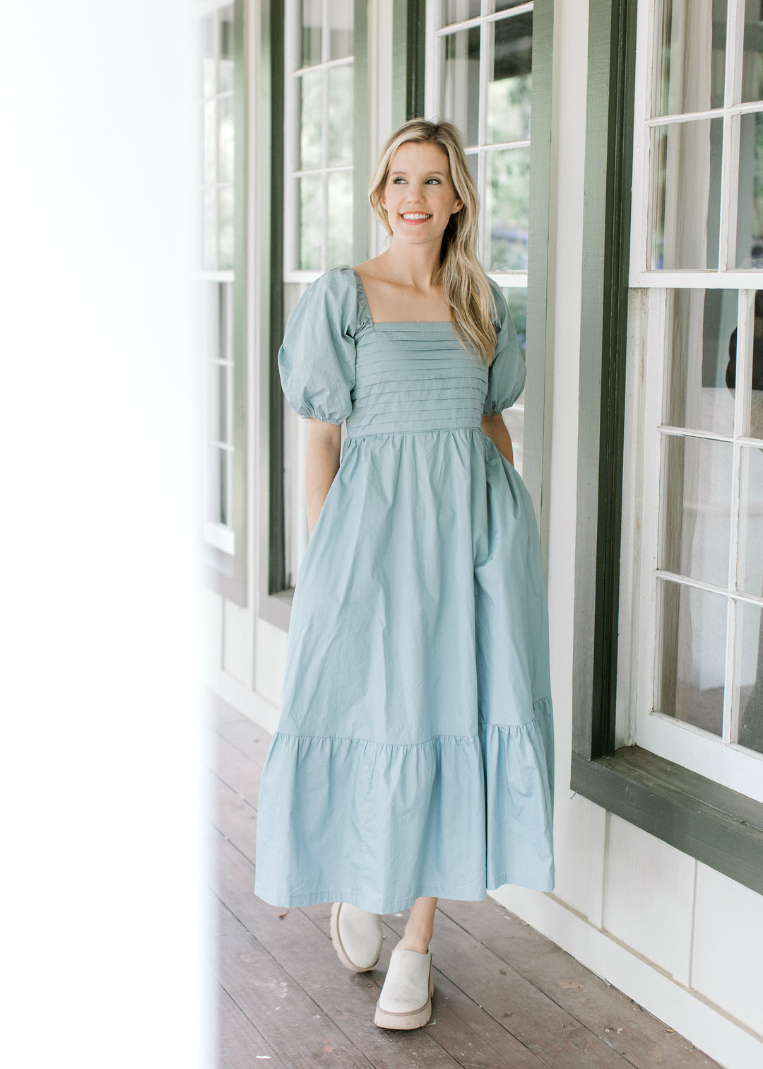 Model wearing mules with a pale blue midi with a pleated bust, pockets and short bubble sleeves.