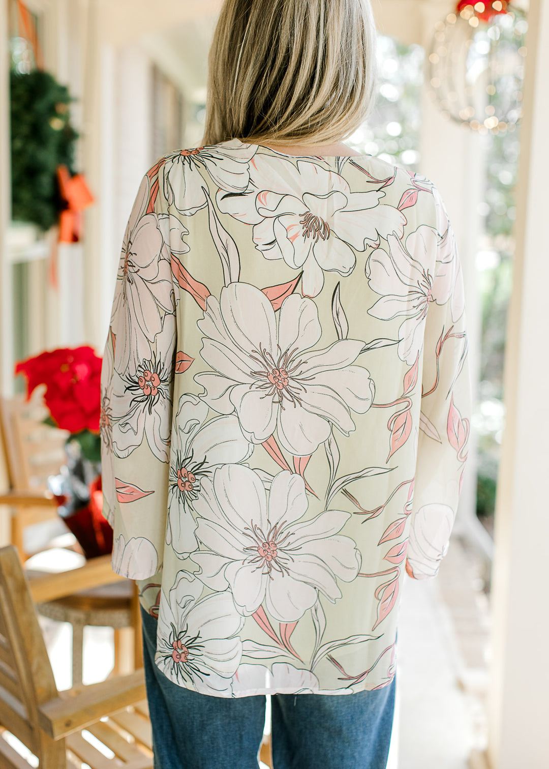 Back view of Model wearing a pale lime top with cream and coral flowers and sheer 3/4 bell sleeves.