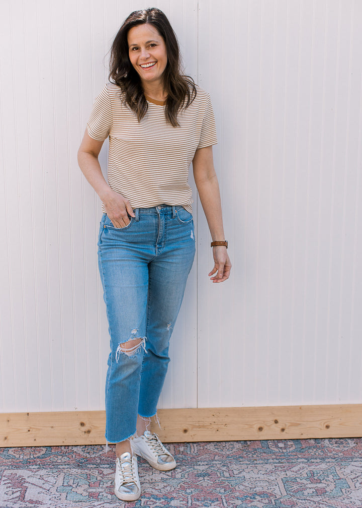 Model wearing jeans, sneakers and a ecru and camel crew neck tee with stripes and short sleeves.