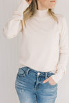 Model wearing a lightweight cream sweater with long sleeves and a mock neckline. 