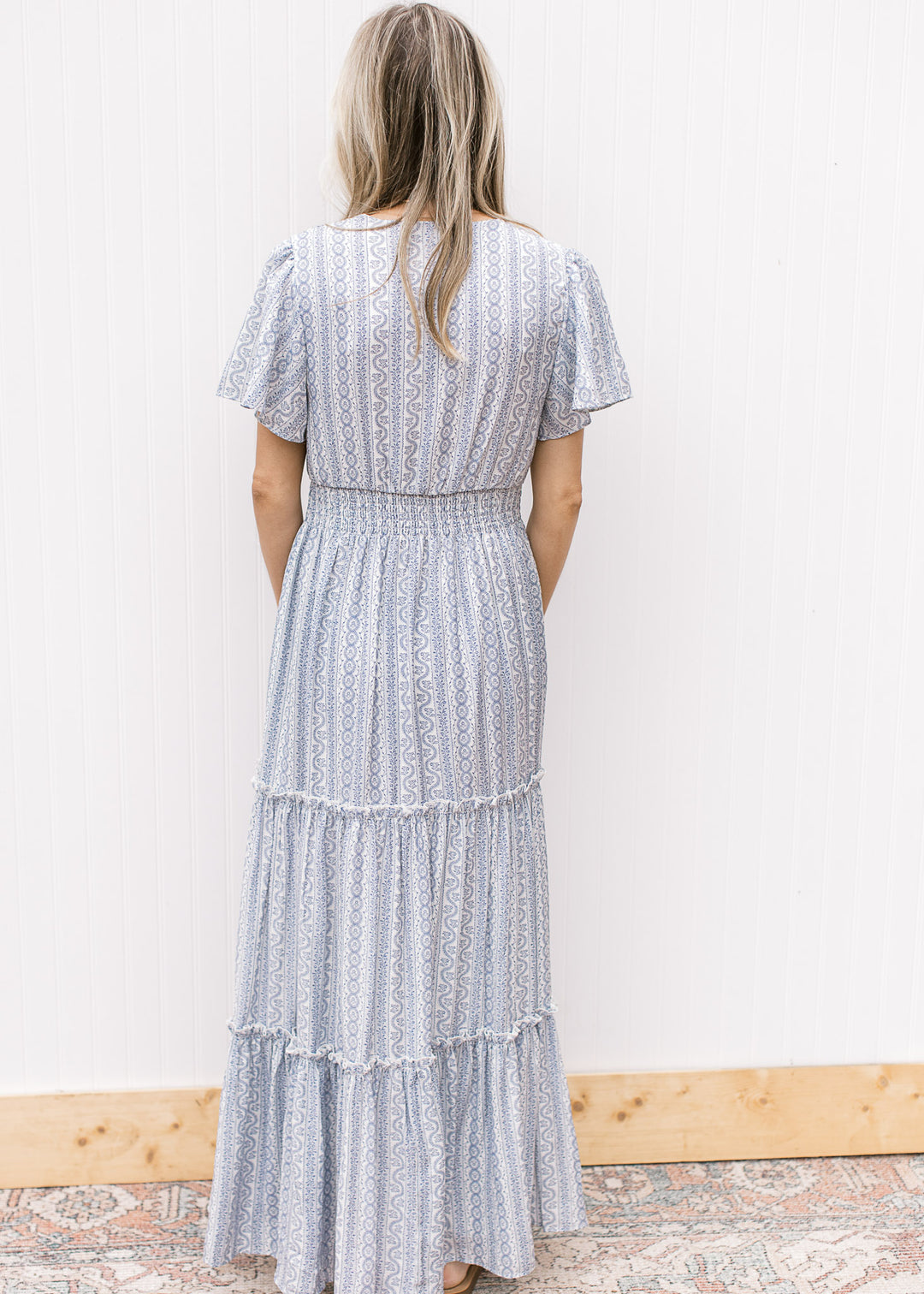 Back view of Model wearing a white maxi with a pale blue print, short sleeves and an elastic waist.