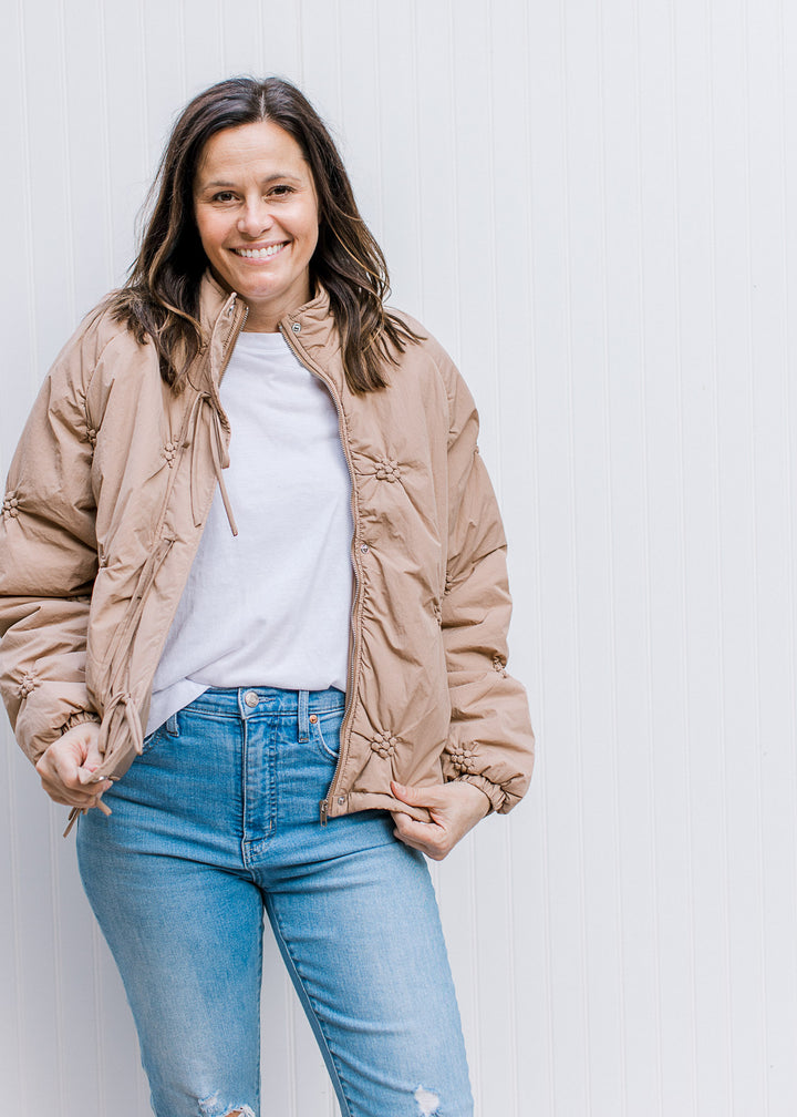 Model wearing a white top with taupe puffer jacket with flower detail and long sleeves.