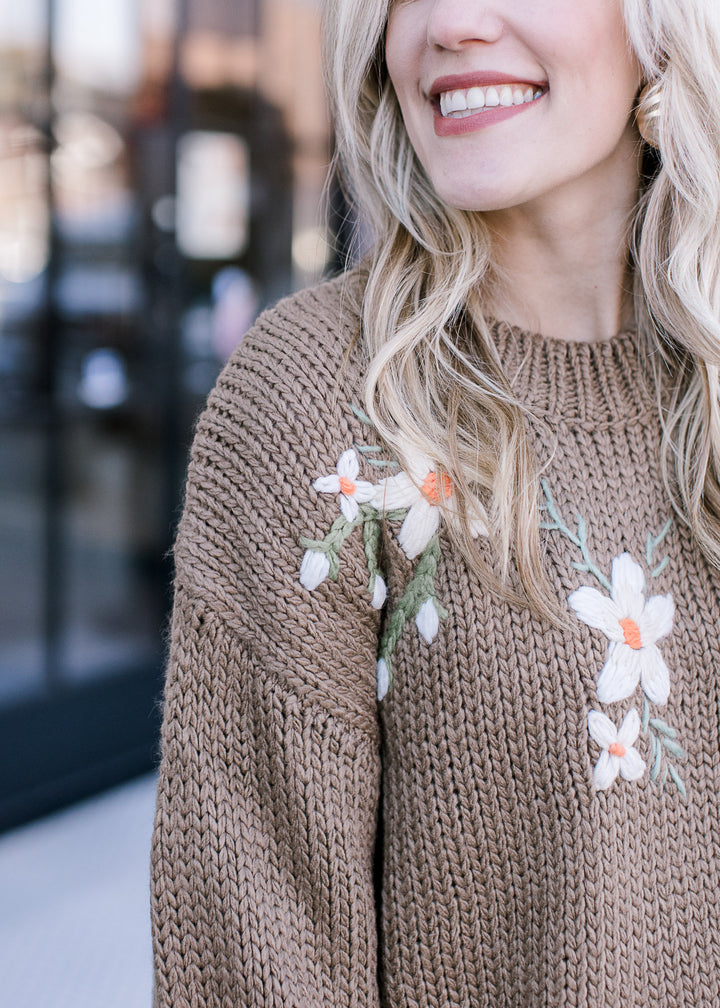 Close up of white embroidered flowers on an olive sweater with bubble long sleeves.