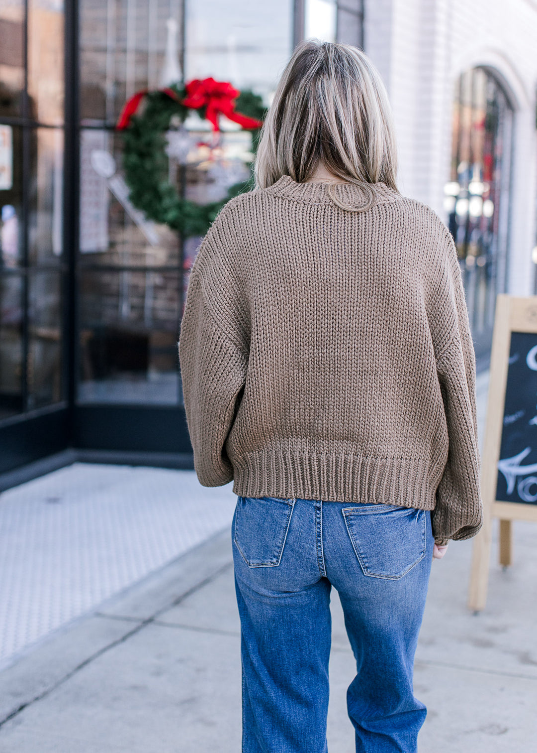 Back view of Model wearing a knit olive green sweater with bubble long sleeves.