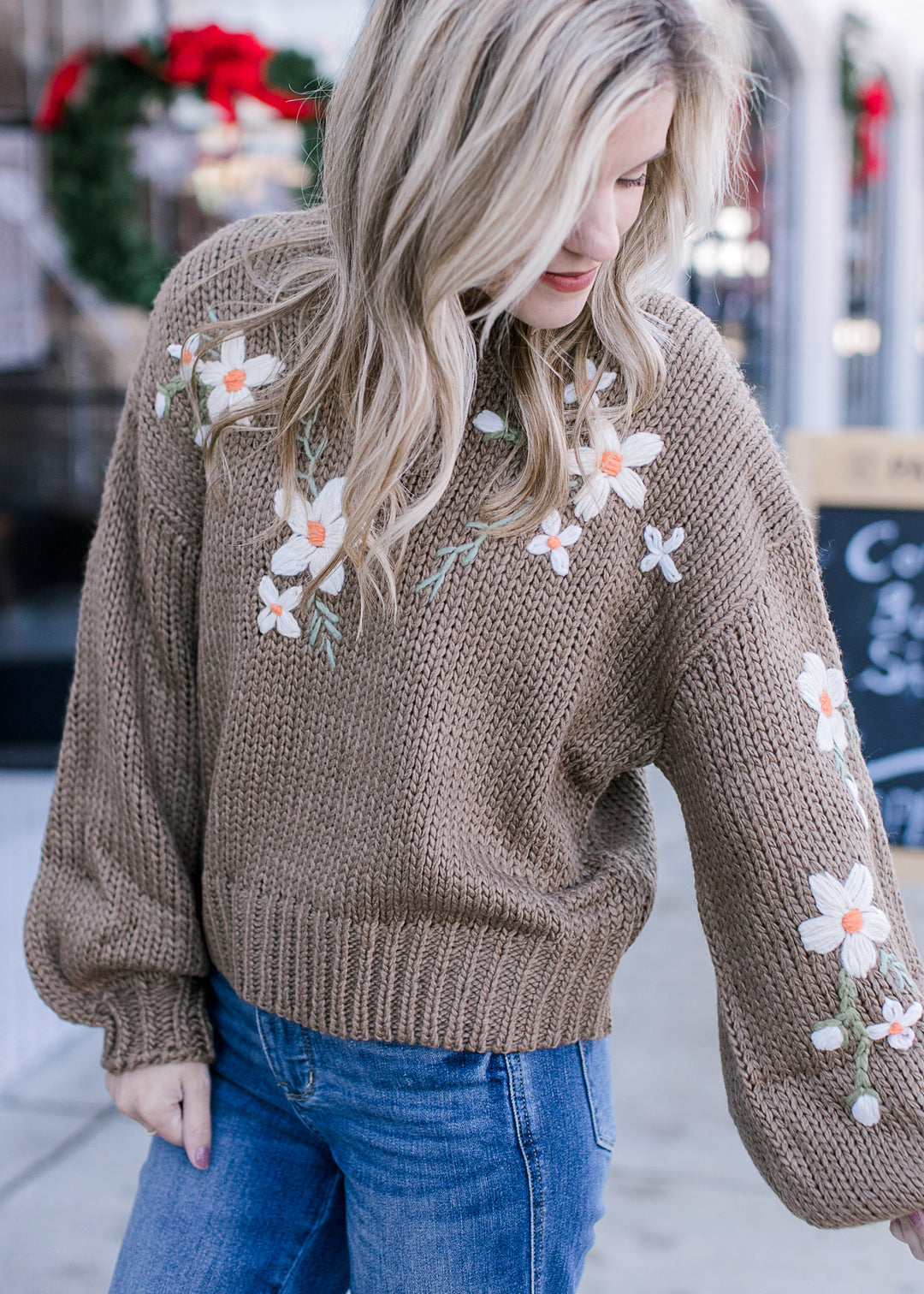 Model wearing an olive green sweater with cream embroidered flowers and bubble long sleeves.
