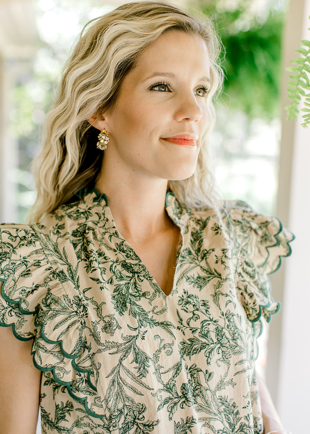 Close up of v-neck and ruffle cap sleeves on a beige top with green floral.