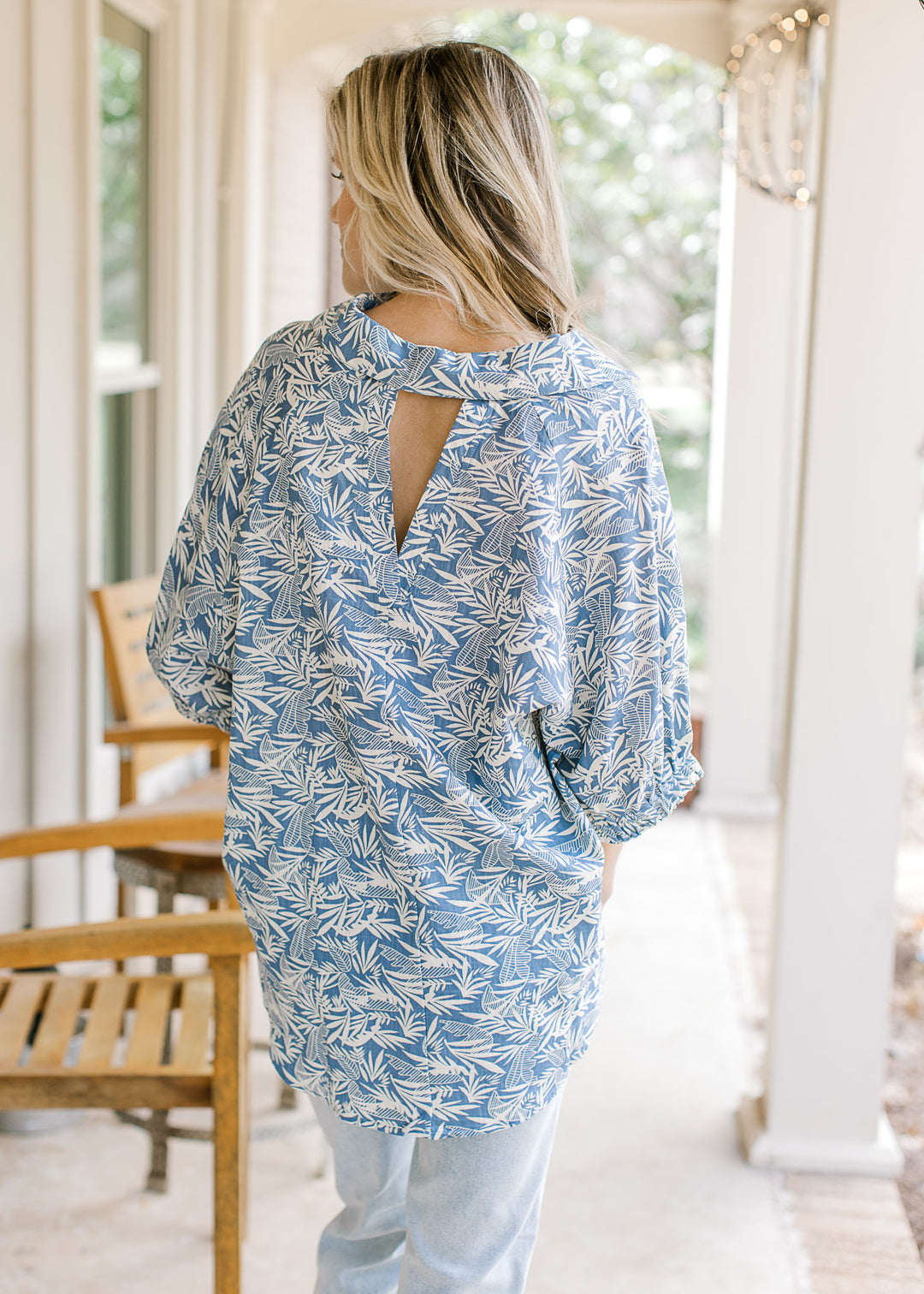 Back view of model wearing a blue top with a cream pattern and a v-neck cut out in back.