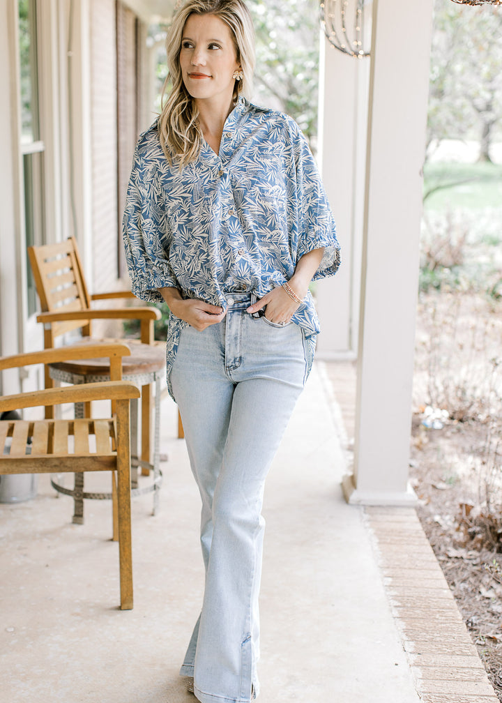 Model wearing jeans and a blue button up top with a cream pattern, collar and short sleeves.