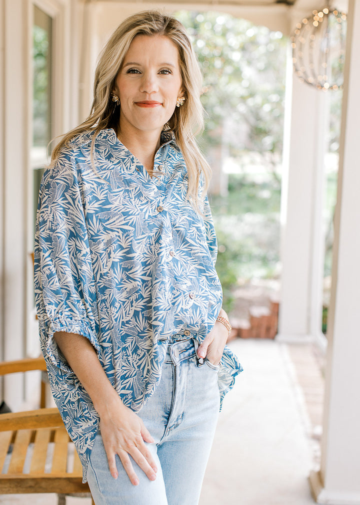 Model wearing a blue button up top with a cream pattern and short sleeves with wide elastic cuff.