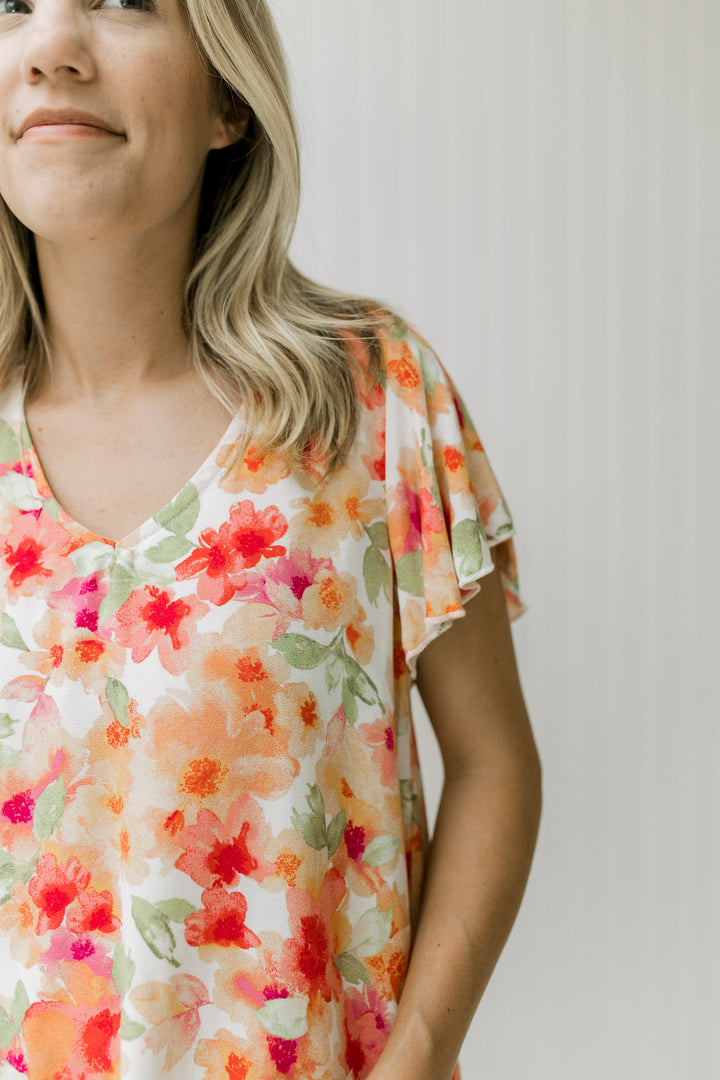 Close up of red, orange and green floral pattern on a white top with a v-neck and short sleeves.