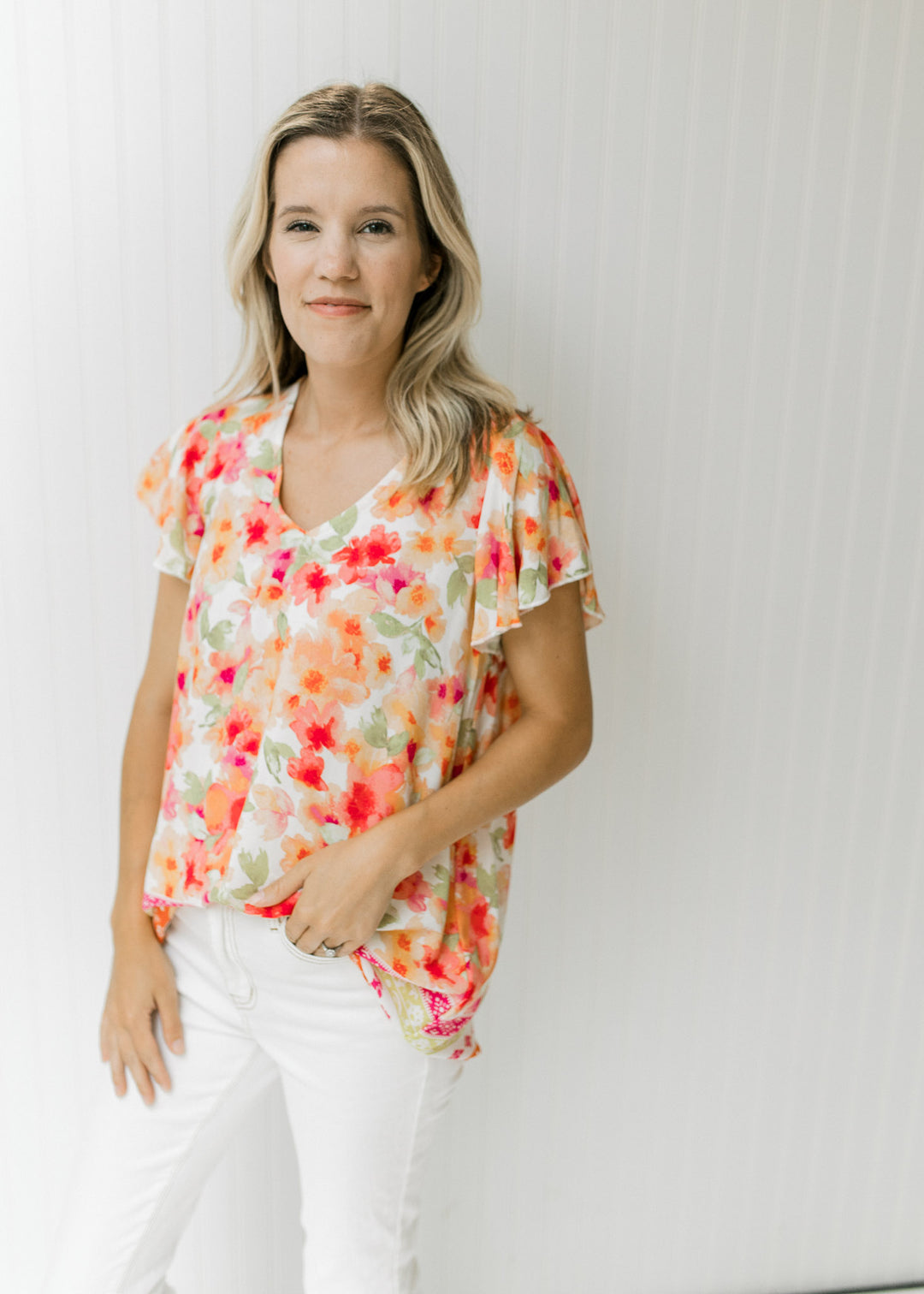 Model wearing a v-neck white top with short sleeves and a red, orange and green floral pattern.