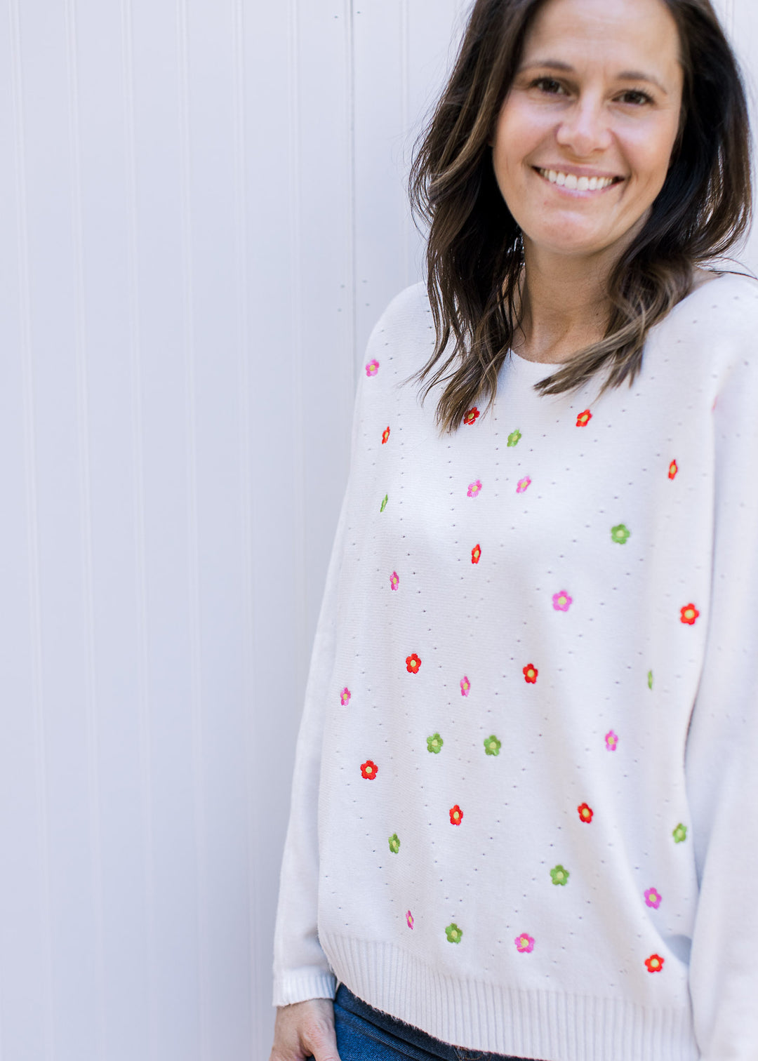 Model wearing a white sweater with colorful embroidered flowers and long sleeves.