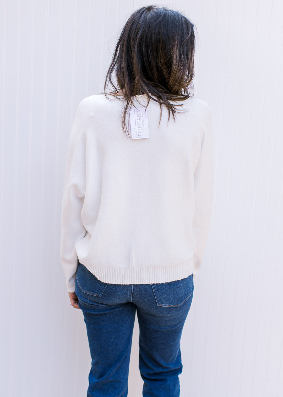 Back view of Model wearing a white sweater with colorful embroidered flowers and long sleeves.