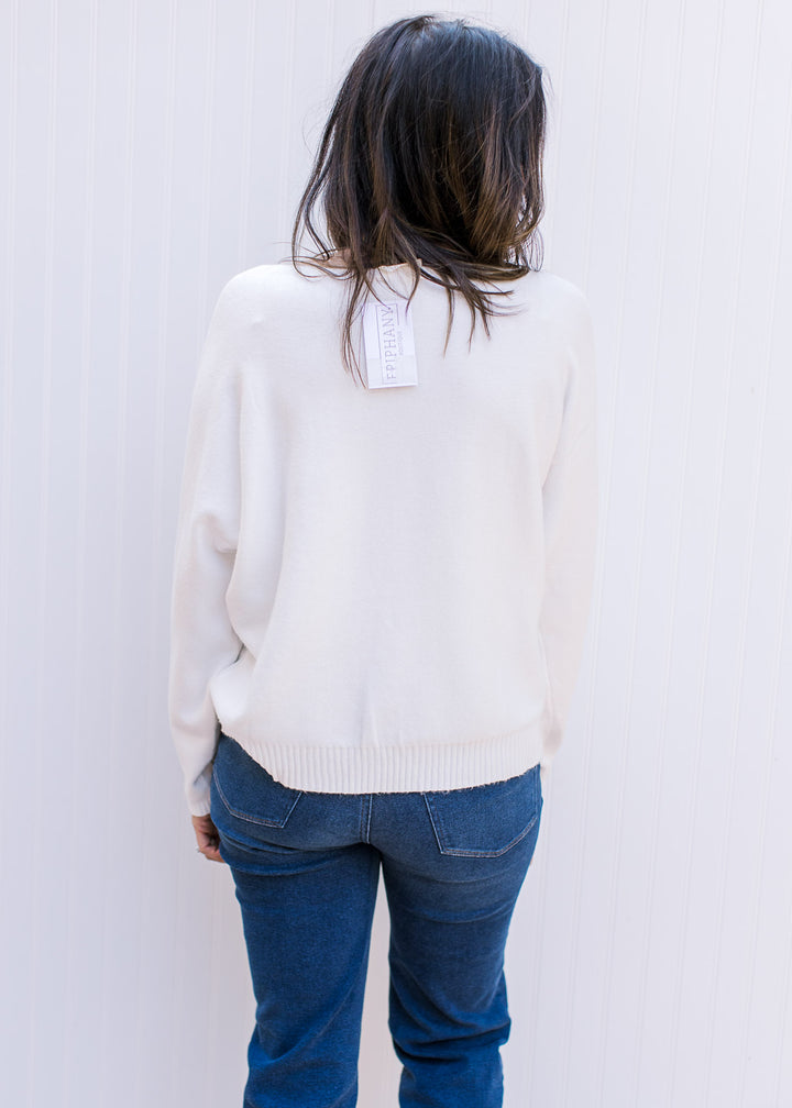 Back view of Model wearing a white sweater with colorful embroidered flowers and long sleeves.
