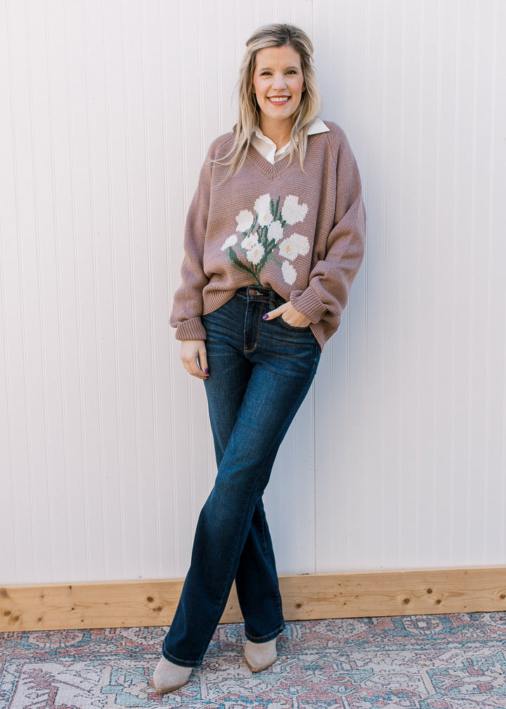 Model wearing jeans, booties and a lavender sweater with white floral bouquet on the front.