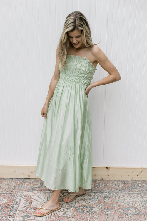 Model wearing a pale green midi with a smocked bust, adjustable straps with a polyester material.