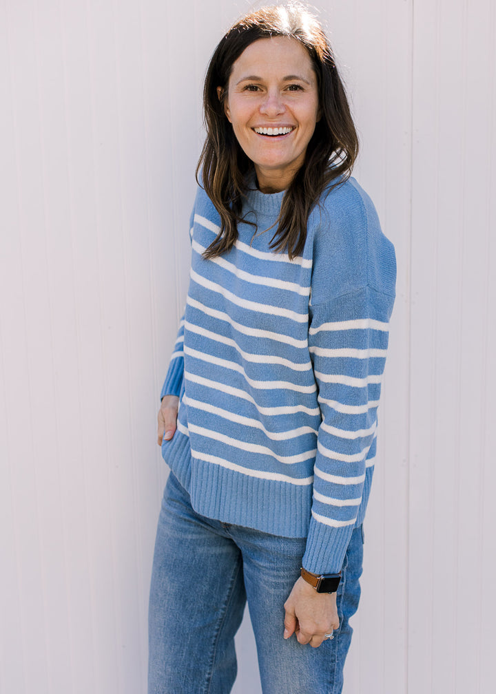 Model wearing a light blue sweater with cream stripes, long sleeves and a round neck.